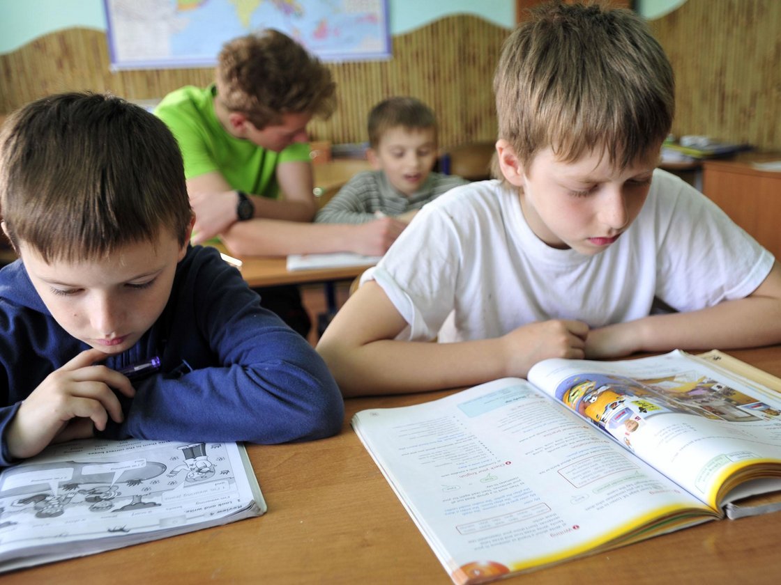 Vier Jungen im Klassenzimmer, zwei im Vordergrund konzentrieren sich intensiv auf ihre offenen Schulbücher.