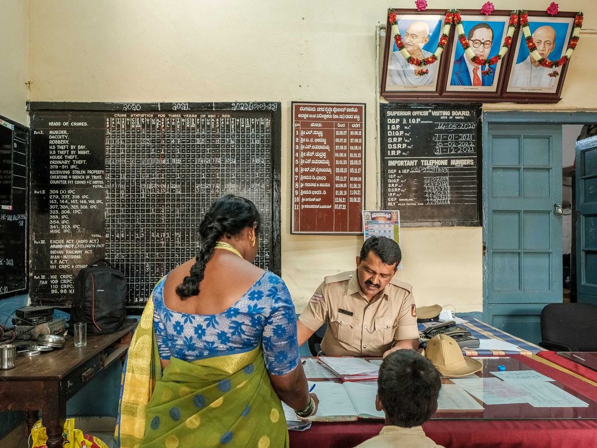 Ein indischer Polizist spricht mit einer Frau und einem Kind in einer Polizeistation mit Kriminalitätsübersichten.