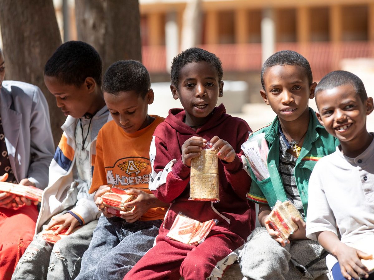Sechs junge Jungen halten verpackte Cracker im Freien, einige lächeln direkt in die Kamera.