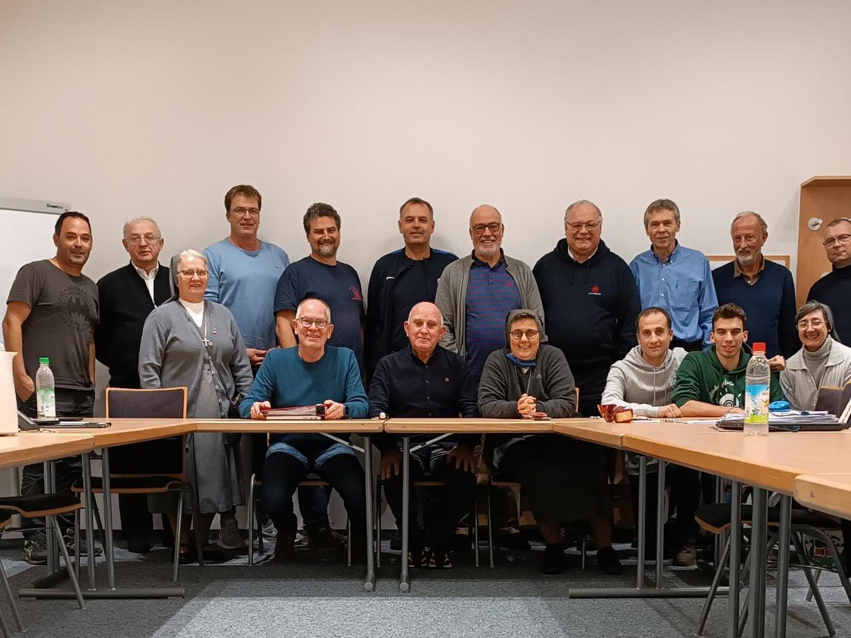 Gruppenfoto von 19 Personen, darunter Männer und Frauen, an einem U-förmigen Tisch in einem Besprechungsraum.