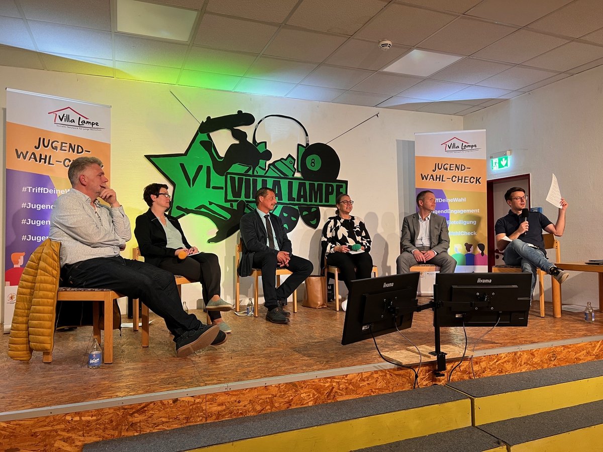 Podiumsdiskussion mit sechs Personen auf einer Bühne vor Bannern des Jugend-Wahl-Checks und dem Villa Lampe Logo.