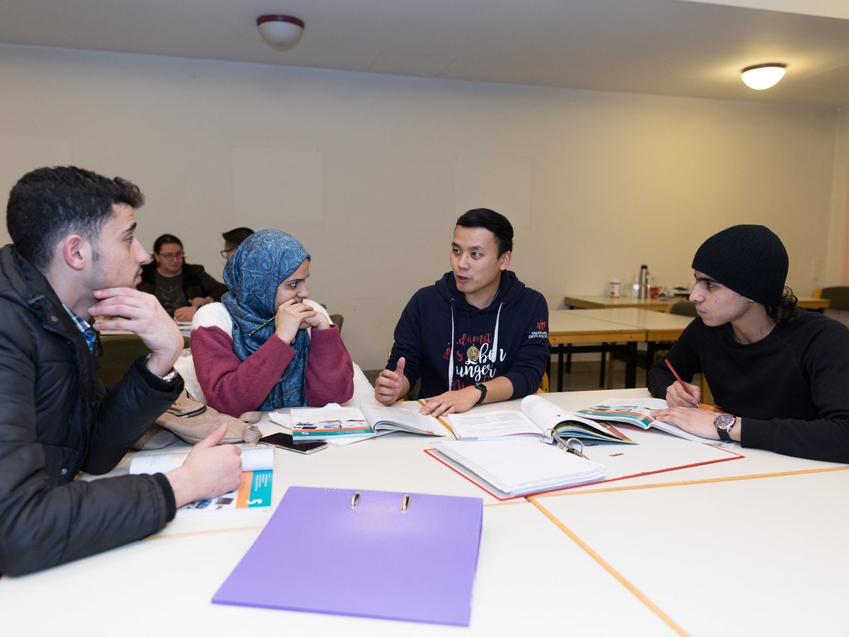 Eine vielfältige Gruppe von vier Studierenden lernt gemeinsam an einem Tisch in einem Klassenzimmer, mit Büchern und Notizen.