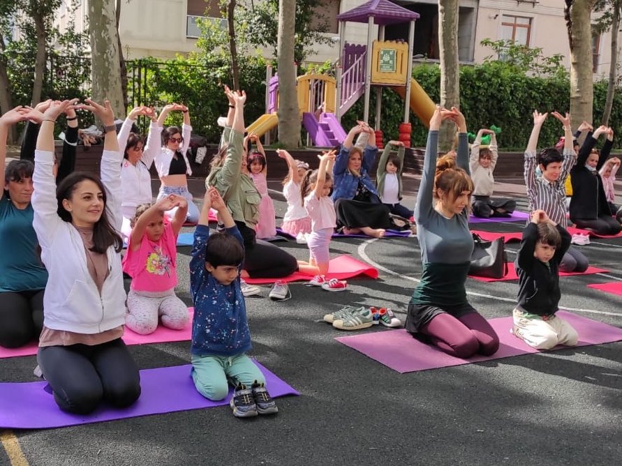 Frauen und Kinder kniend auf Yogamatten im Freien, die Arme über dem Kopf erhoben in einer Gruppe dehnen.