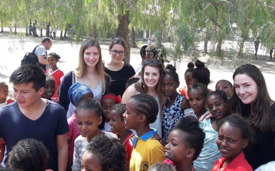 Eine vielfältige Gruppe lächelnder junger Erwachsener und Kinder, die im Freien in der Sonne versammelt sind.