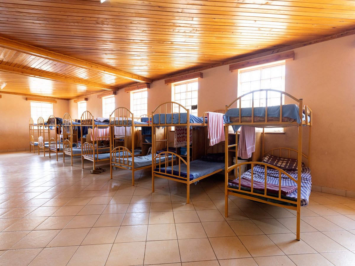 Schlafsaal mit vielen gelben Metall-Etagenbetten, blauen Matratzen und Handtüchern, unter einer hellen Holzdecke.