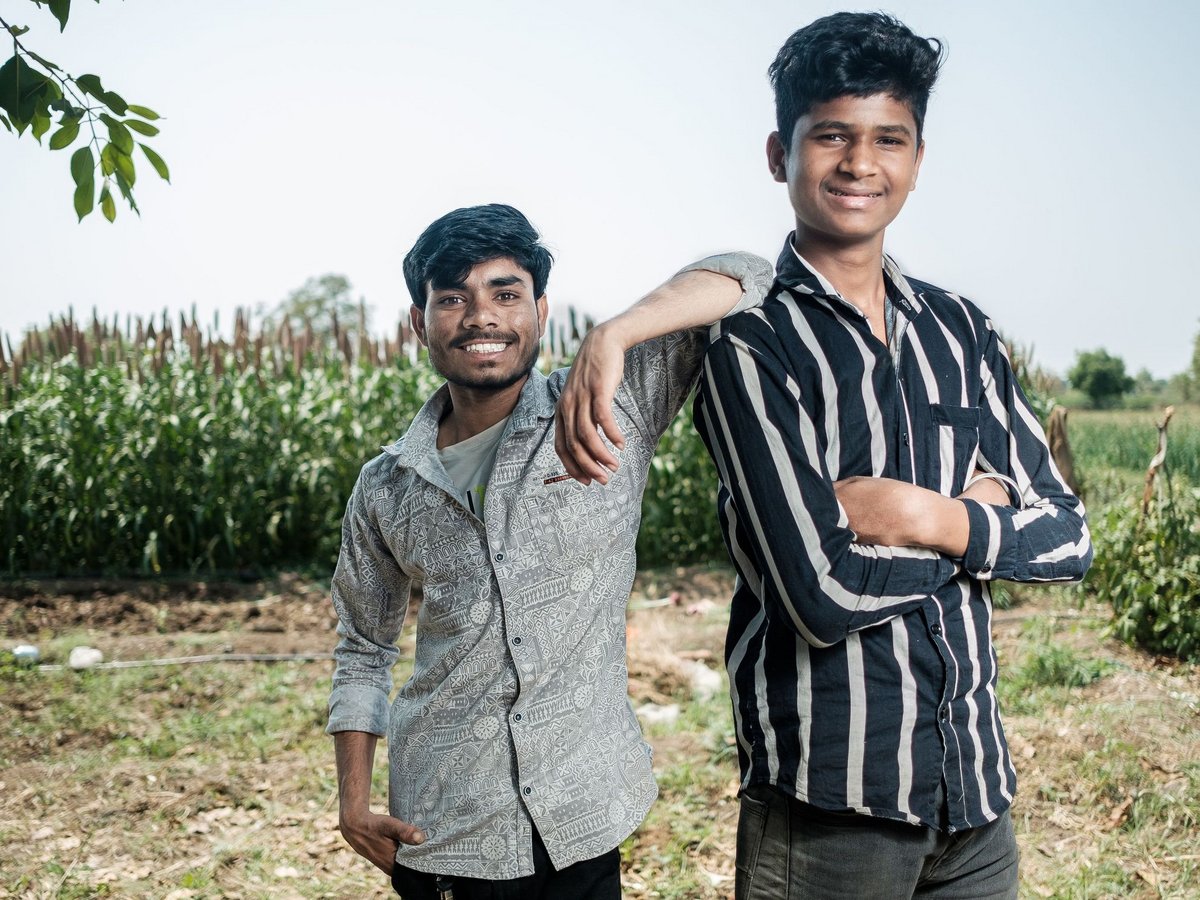 Zwei Freunde, junge indische Männer, lächeln und posieren auf einem Hirsefeld.