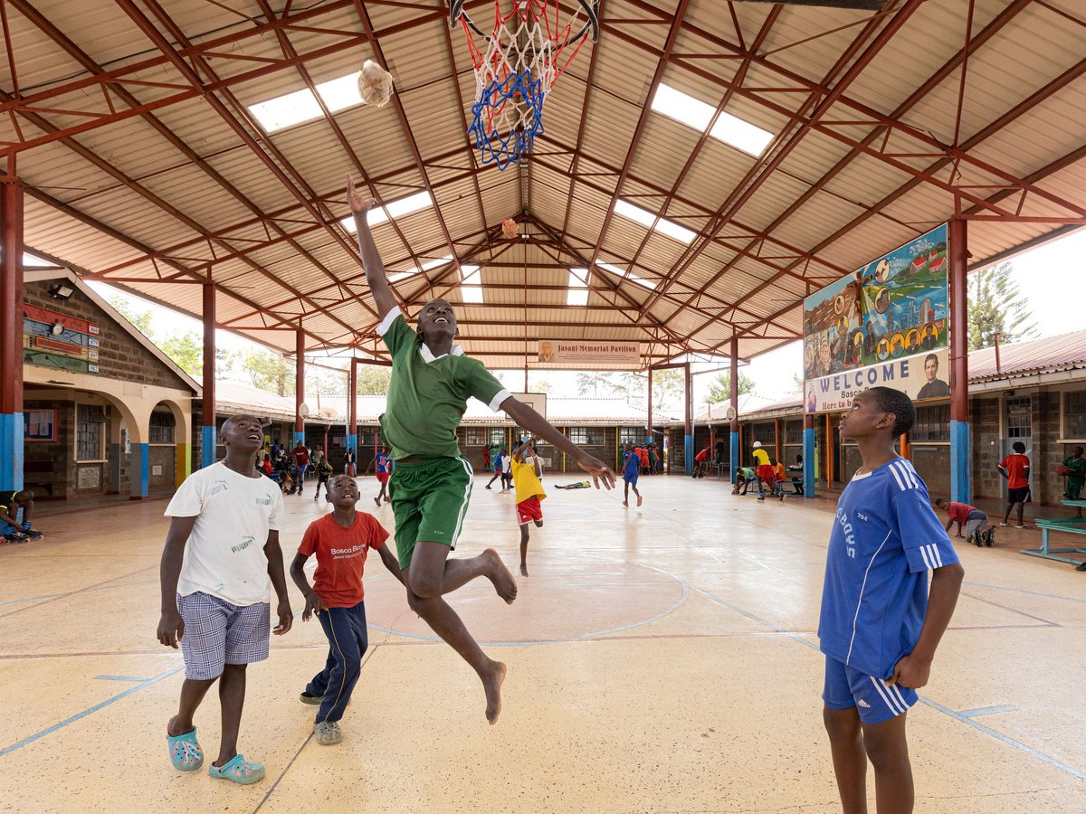 Ein barfüßiger Junge in grüner Sportkleidung springt hoch, um einen improvisierten Ball zu dunken.