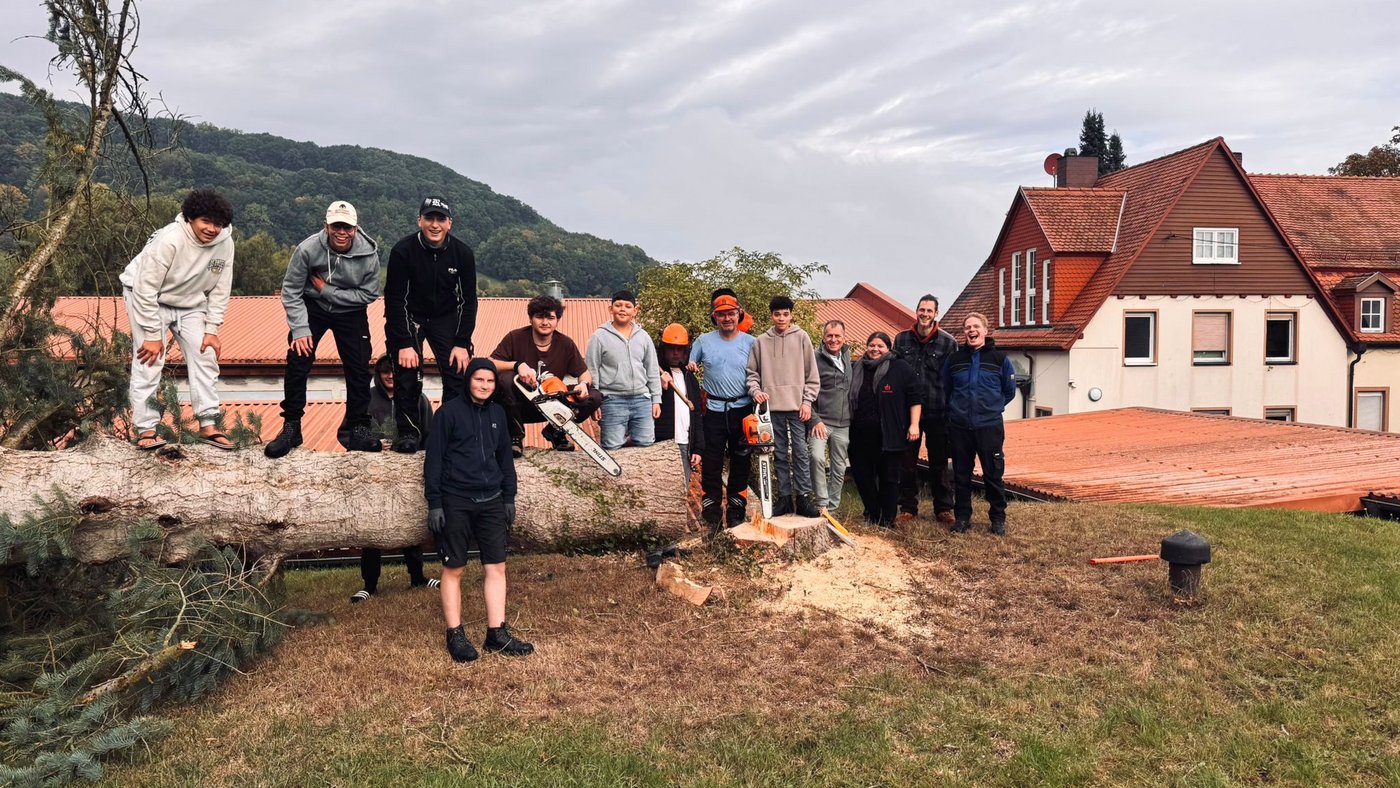 Jugendliche und Betrauer mit Sägen und einem gefällten Baum bereiten Platz für neuen Spielplatz vor