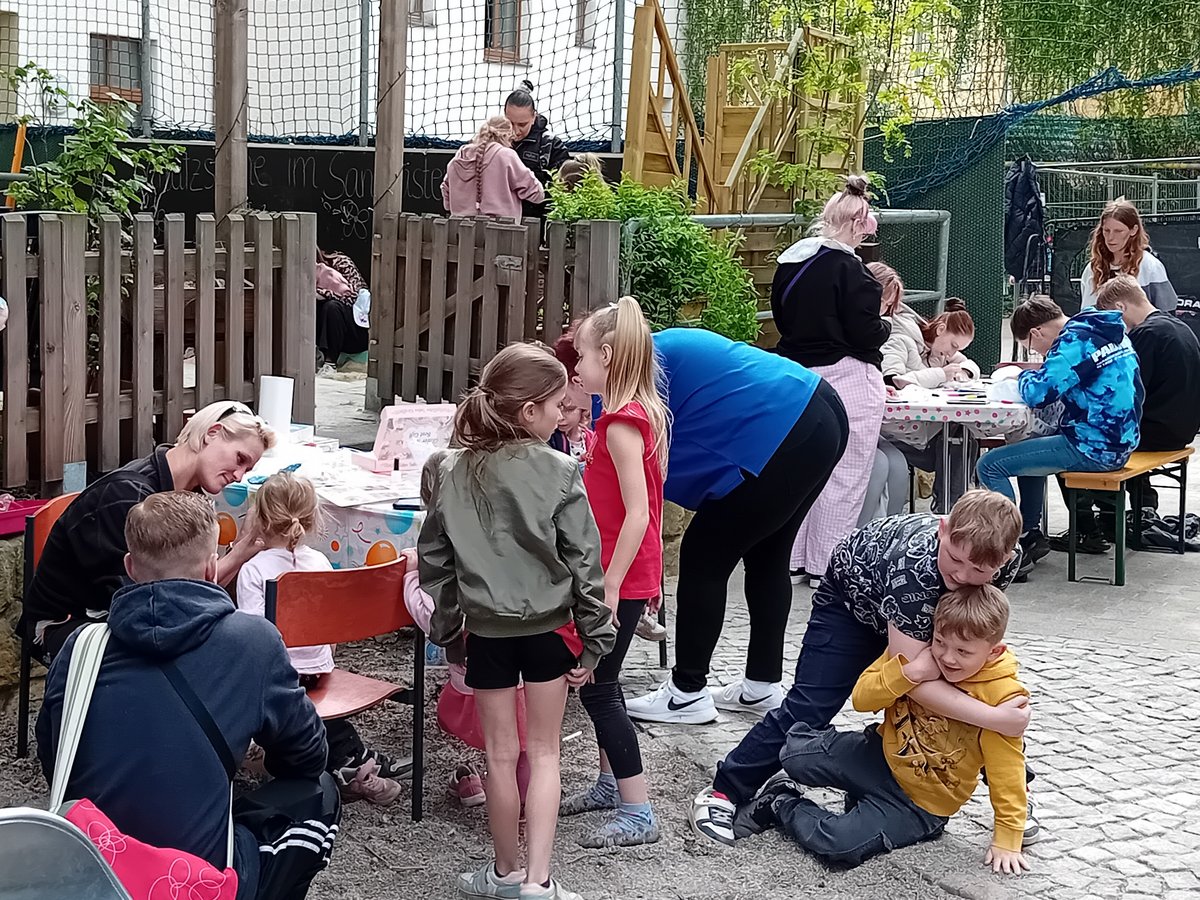 Ein lebhaftes Outdoor-Event mit Erwachsenen und Kindern. Einige basteln an Tischen, andere spielen auf dem Boden.