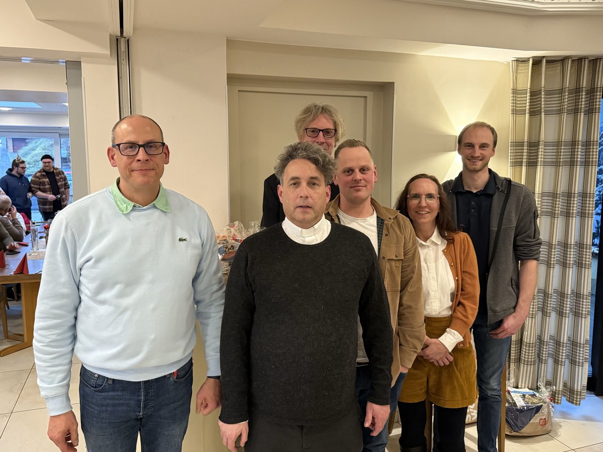 Eine Gruppe von sechs lächelnden Erwachsenen (fünf Männer, eine Frau) posiert für ein Foto bei einer Indoor-Veranstaltung.