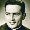 Halbporträt eines lächelnden jungen Priesters mit dunklem Haar und Kollar in Sepia-Tönen.