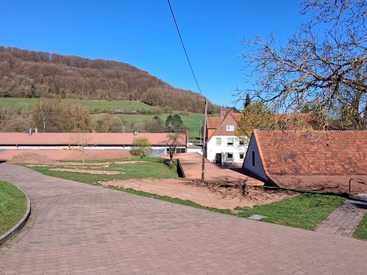 Gelände mit Straße, Wiese und Häusern und vorbereitem Bereich für neuen Spielplatz