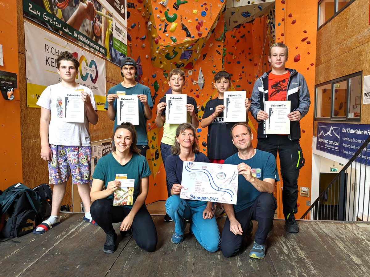 Gruppenfoto in einer Kletterhalle: Fünf Jungen halten Urkunden, zwei Frauen und ein Mann knien mit einem Poster, ein Mann steht.