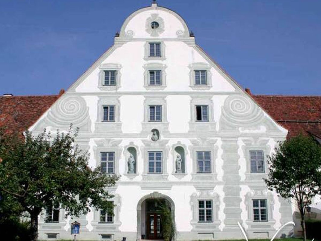 Barockes Giebelfassadengebäude in Weiß mit grauen Verzierungen, Fenstern und Statuen unter blauem Himmel.