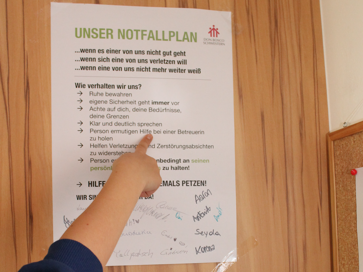 Ein Kind zeigt mit dem Finger auf einen Notfallplan der Don Bosco Schwestern mit Verhaltensregeln für Notfälle.