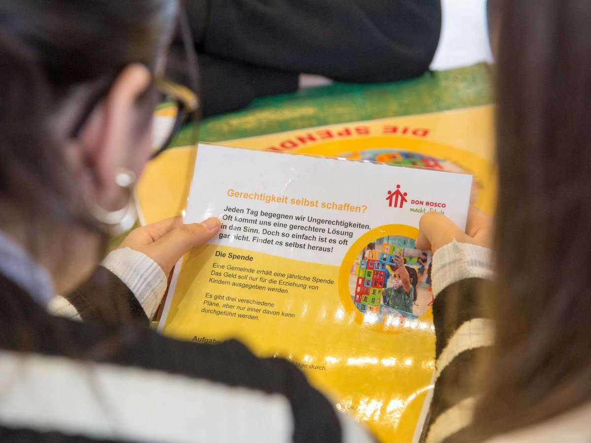 Eine Person hält ein Don Bosco Flugblatt mit dem Titel „Gerechtigkeit selbst schaffen?“ über Spenden für Kindererziehung.