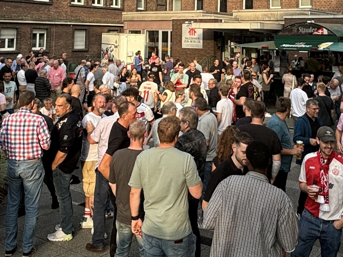 Viele Menschen versammeln sich im Freien bei einem Fest mit Essens- und Getränkeständen, darunter ein Stauder-Ausschank.