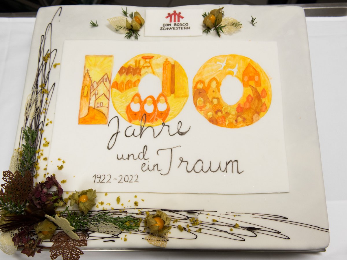 Kuchen zum 100-jährigen Jubiläum der Don Bosco Schwestern. Aufschrift '100 Jahre und ein Traum 1922-2022' mit Nonnen und Gebäuden.