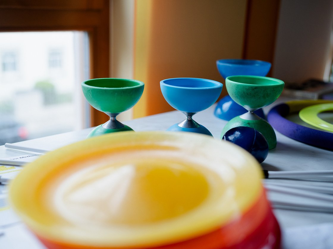 Bunte Diabolos in Grün, Blau und Gelb liegen mit Papieren und Stäben auf einem Tisch nahe eines Fensters.