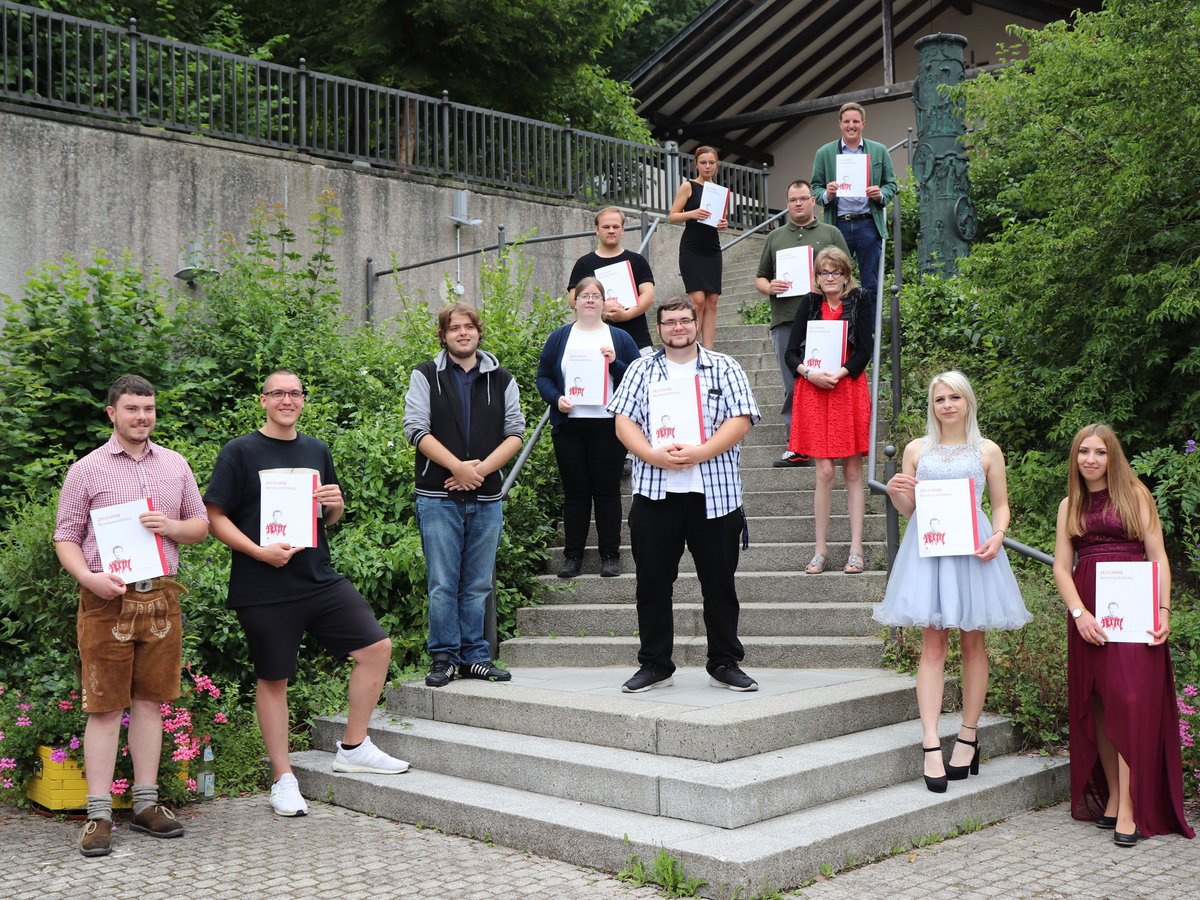 Eine Gruppe Absolventen hält ihre Zeugnisse der Berufsausbildung auf einer Steintreppe im Freien.