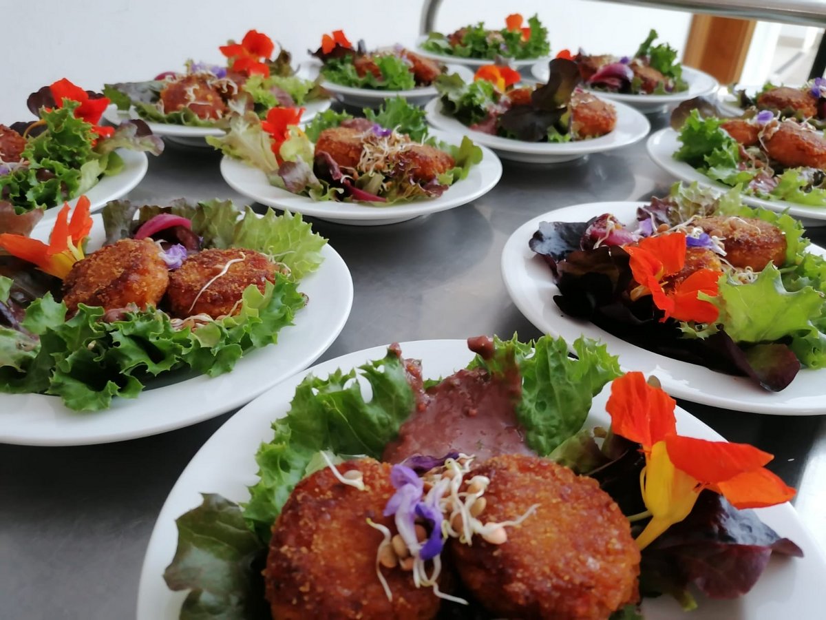 Teller mit goldbraunen Kroketten auf Salatblättern, garniert mit essbaren Blüten und Sprossen auf Metallfläche.