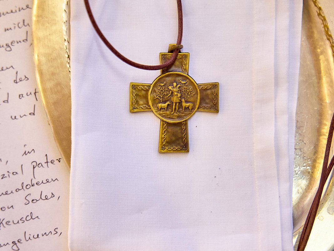 Religiöses Kreuz und Dokument Goldenes Kreuz mit Hirten- und Schafmotiv auf weißem Tuch, goldener Platte und handschriftlichem Brief.