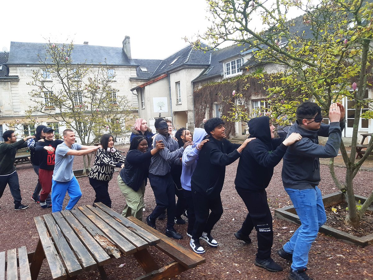 Schüler bilden eine Reihe, einige mit verbundenen Augen, spielen ein Vertrauensspiel draußen im Hof.