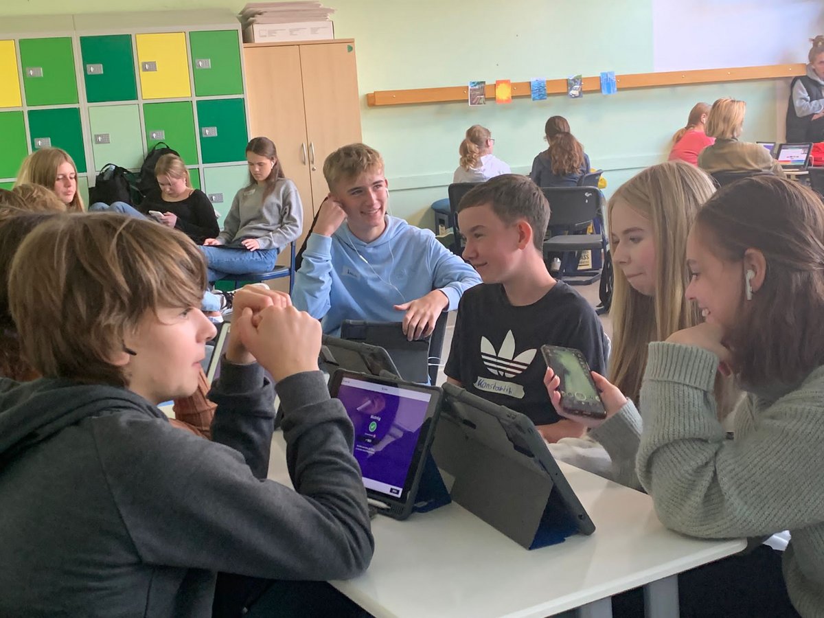 Eine Gruppe von Schülern nutzt aktiv Tablets und Smartphones in einem Klassenzimmer für gemeinsames Lernen.