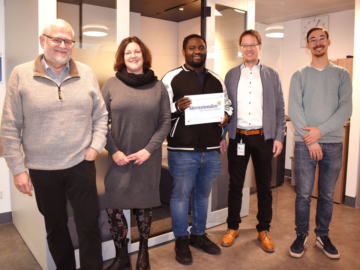 Fünf lächelnde Personen, eine hält ein 'Sternstunden'-Schild für Kinderhilfswerk im Büro.
