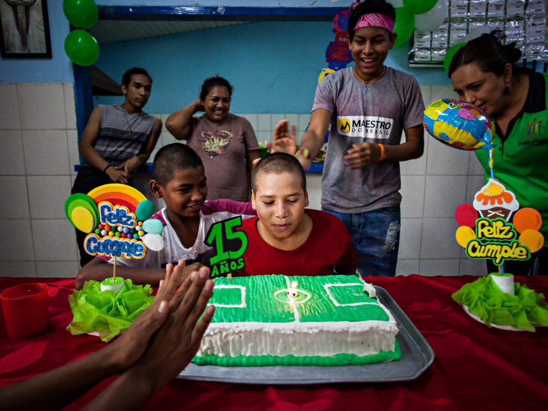 Ein Junge bläst eine Kerze auf einem Fußballkuchen aus, umgeben von Familie und Freunden bei seinem 15. Geburtstag.