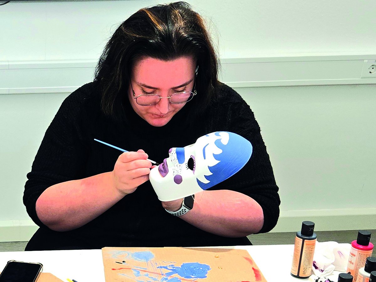 Eine Frau bemalt eine weiße Maske mit blauen und lila Mustern.