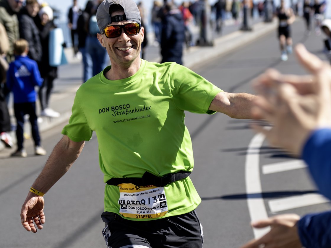 Ein lächelnder Läufer im grünen T-Shirt und Sonnenbrille streckt beim Bonner Marathon die Hand zum High-Five aus.