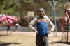Ein lächelnder Junge in einem 'JAMAICA'-Trikot auf einem Spielplatz. Im Hintergrund sind undeutlich spielende Kinder und Spielgeräte zu sehen.