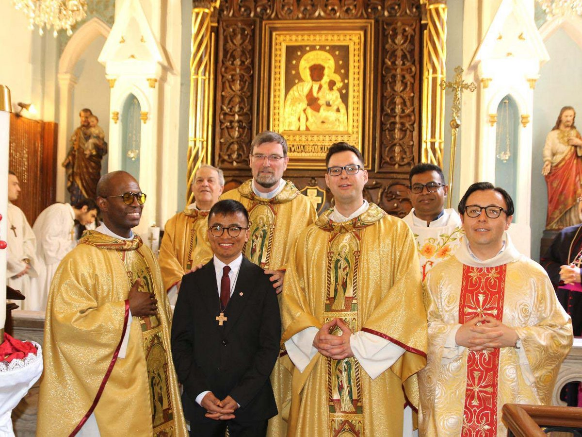Lächelnde Priester und ein Mann im Anzug in einer Kirche mit goldenem Altar und religiöser Kunst.