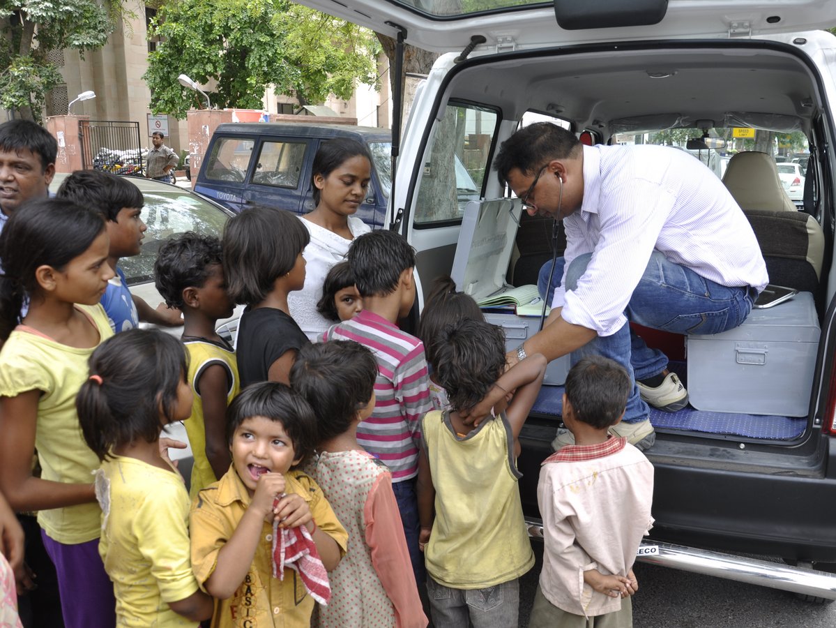 Ein Mann interagiert mit Kindern aus dem Heck eines weißen Lieferwagens, wahrscheinlich für mobile Gemeinde- oder Gesundheitsdienste.