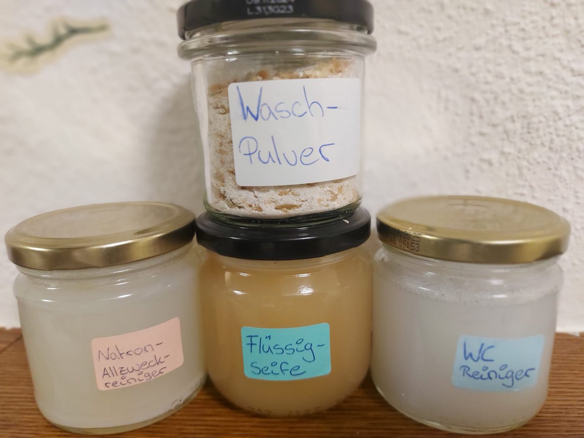 Vier beschriftete Gläser mit selbstgemachten Reinigungsprodukten: Waschpulver, Natron-Allzweck-Reiniger, Flüssigseife und WC-Reiniger.