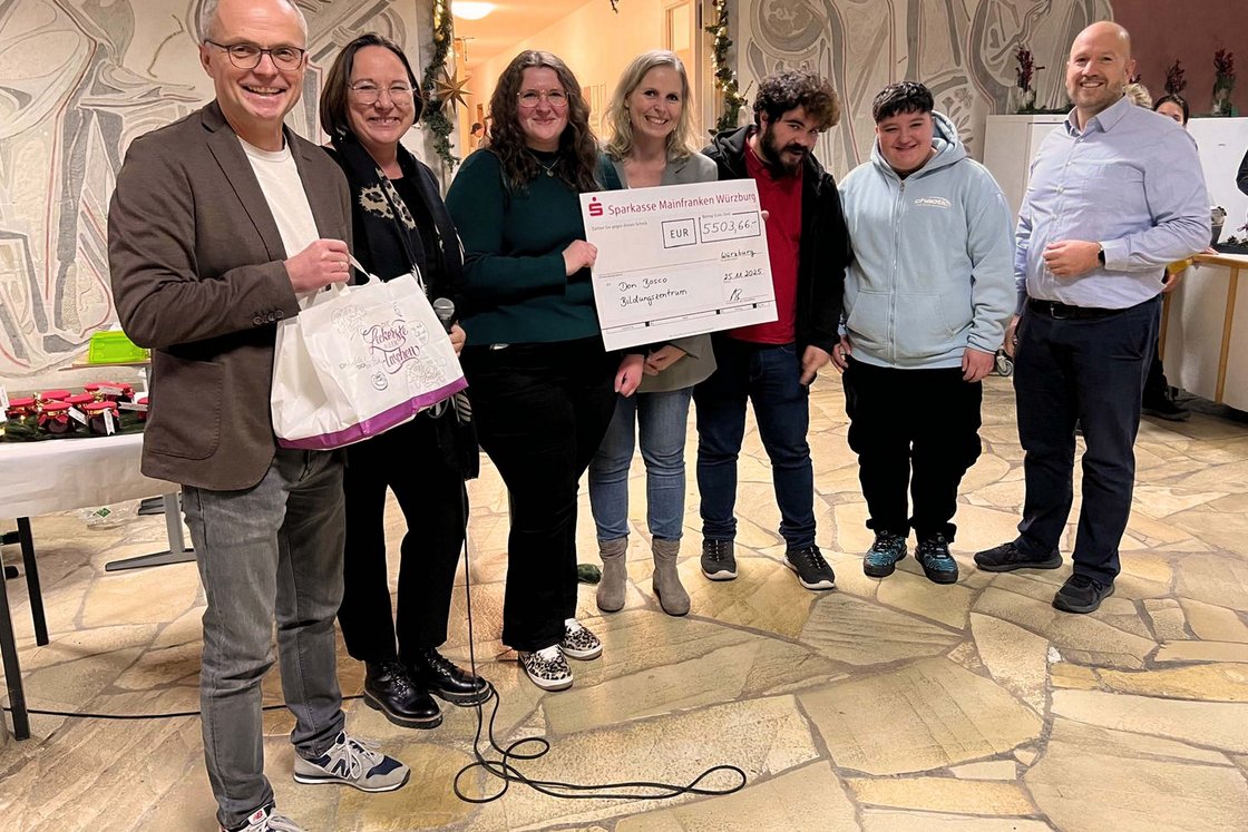 Sieben Personen, darunter Bankvertreter und Don Bosco Mitglieder, lächeln bei der Scheckübergabe über 5503,66 EUR.