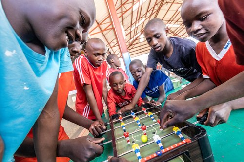Afrikanische Kinder spielen Tischfußball, zeigen Engagement und Freude. Mehrere Jungen verschiedenen Alters konzentrieren sich auf das Spiel.