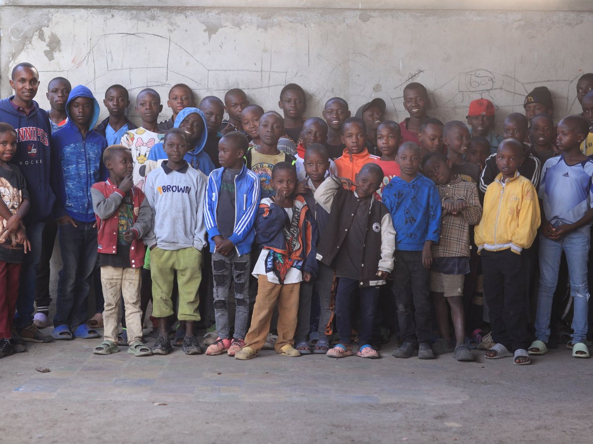 Eine große Gruppe lächelnder Kinder und einiger Erwachsener posiert für ein Gruppenfoto vor einer Betonwand.