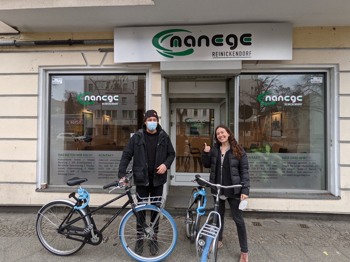 Zwei Personen mit blau bereiften Fahrrädern posieren lächelnd vor dem nancgc Reinickendorf Büro, einer mit Daumen hoch.