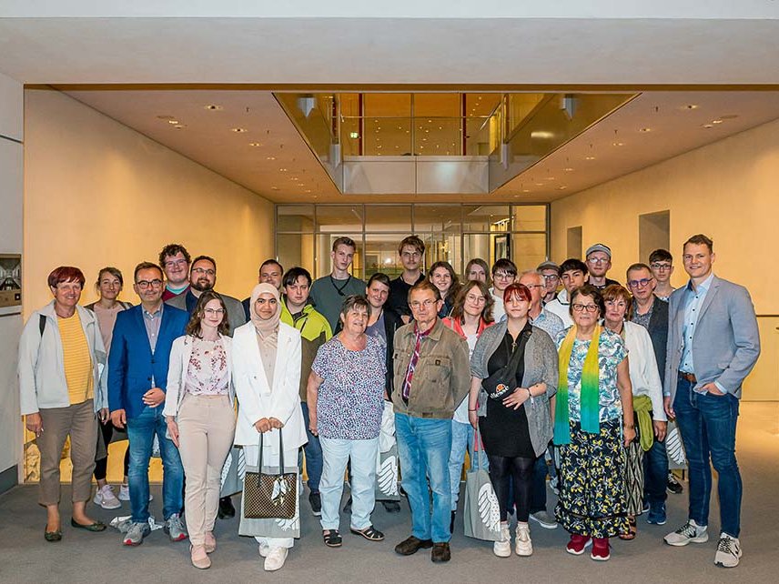 Eine vielfältige Gruppe von Menschen jeden Alters posiert für ein Foto in einem modernen Gebäude.