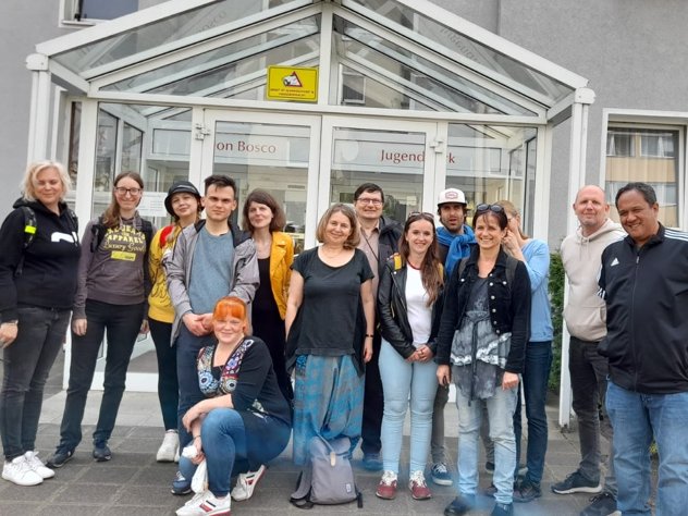 Vielfältige Gruppe von Erwachsenen posiert lächelnd vor dem Eingang des Don Bosco Jugendwerks.