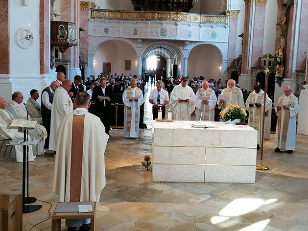 Priester und Gemeinde bei einem Gottesdienst in einer großen, reich verzierten Kirche am Altar.
