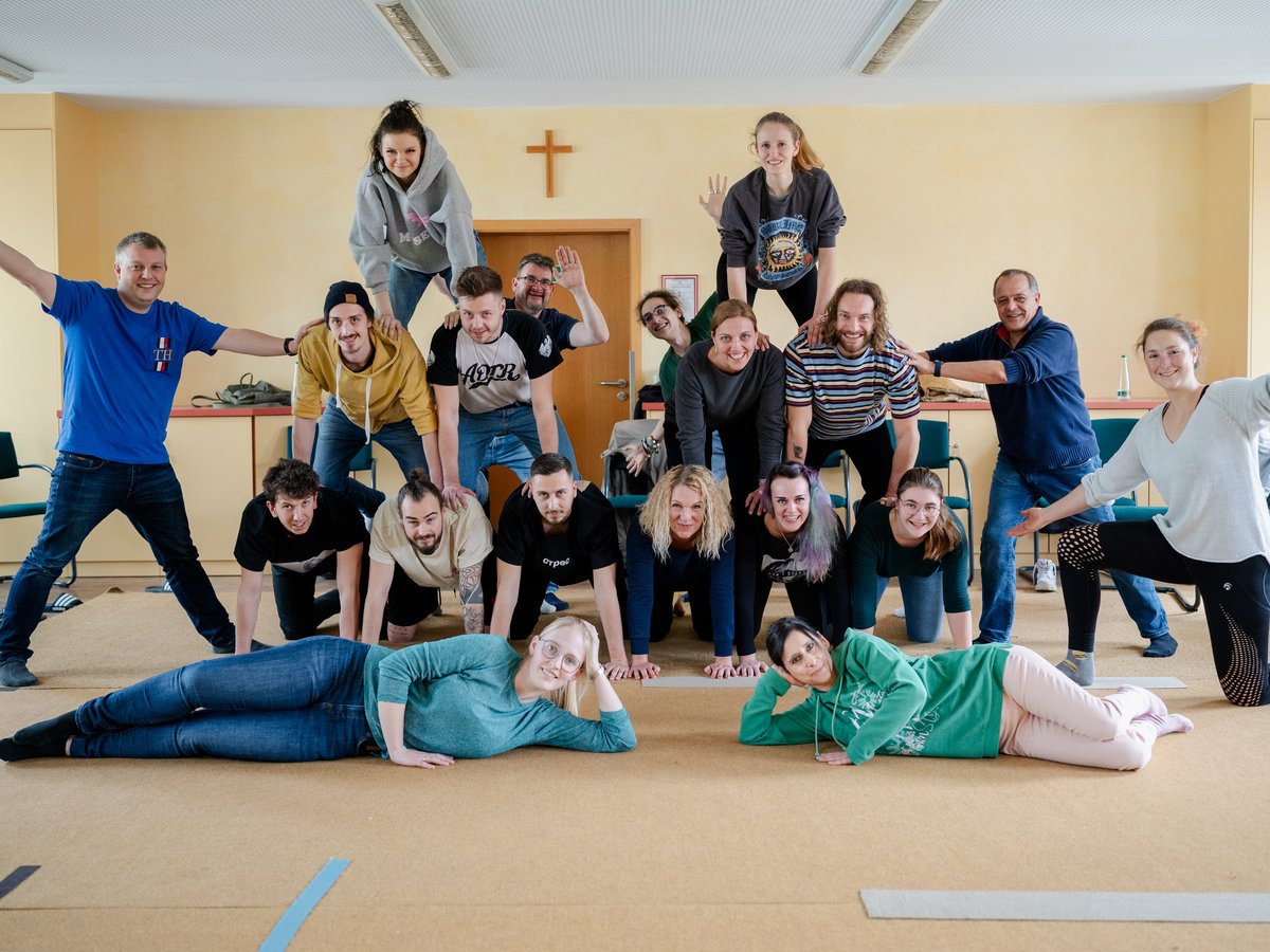 Eine Gruppe von Menschen lächelt, während sie eine kreative menschliche Pyramide in einem Raum bilden.