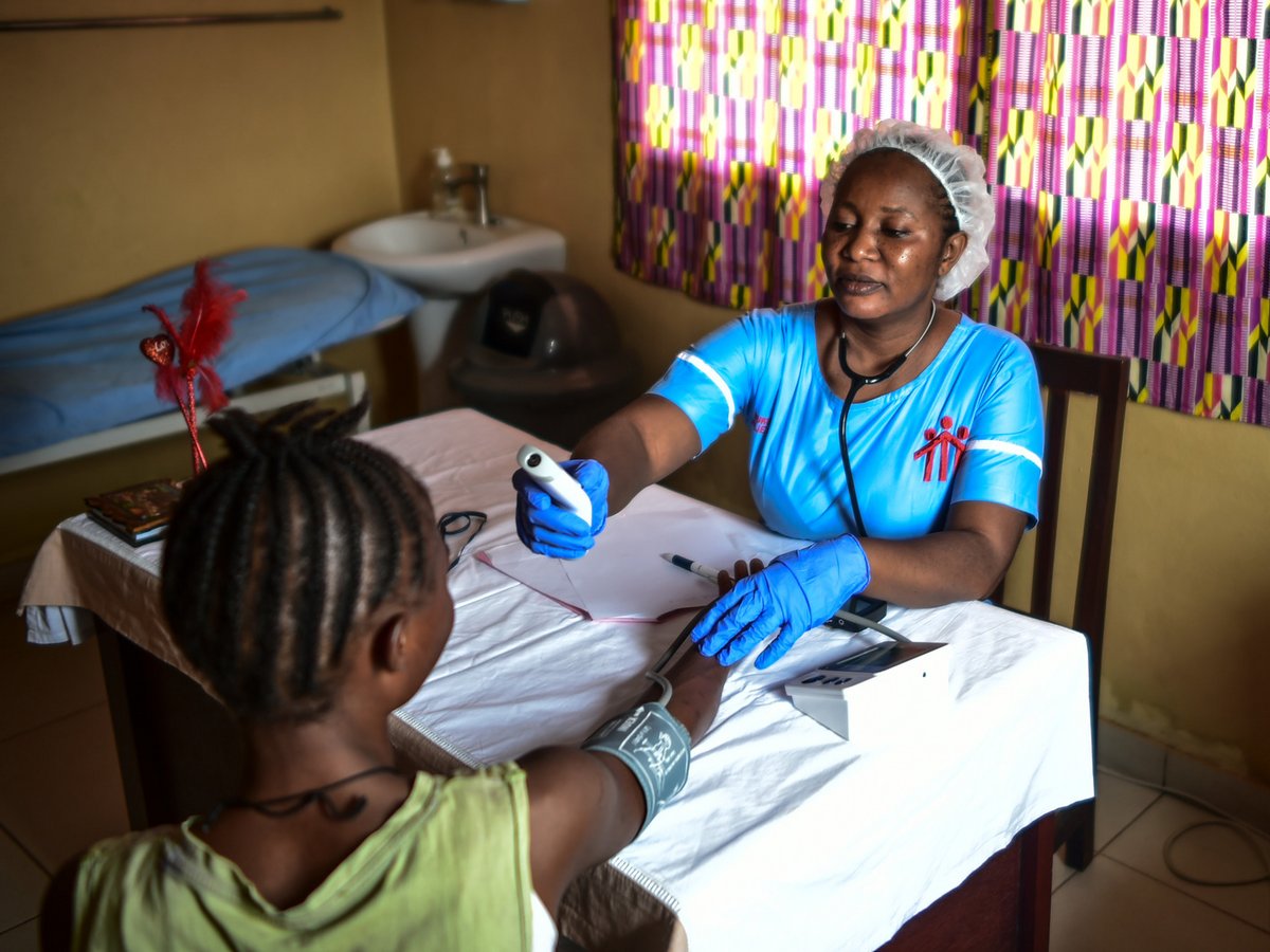 Eine Krankenschwester untersucht ein Kind und misst Temperatur und Blutdruck an dessen Arm.