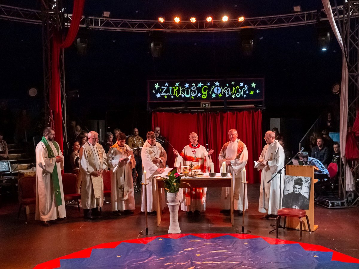 Priester halten einen Gottesdienst im Zirkus Giovanni ab, mit Altar, Kerzen und einer Abbildung von Don Bosco.