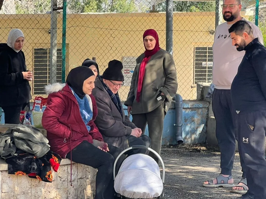 Im Freien versammelte Gruppe von Menschen, darunter Frauen mit Kopftüchern, Männer und ein Baby in einem Kinderwagen.