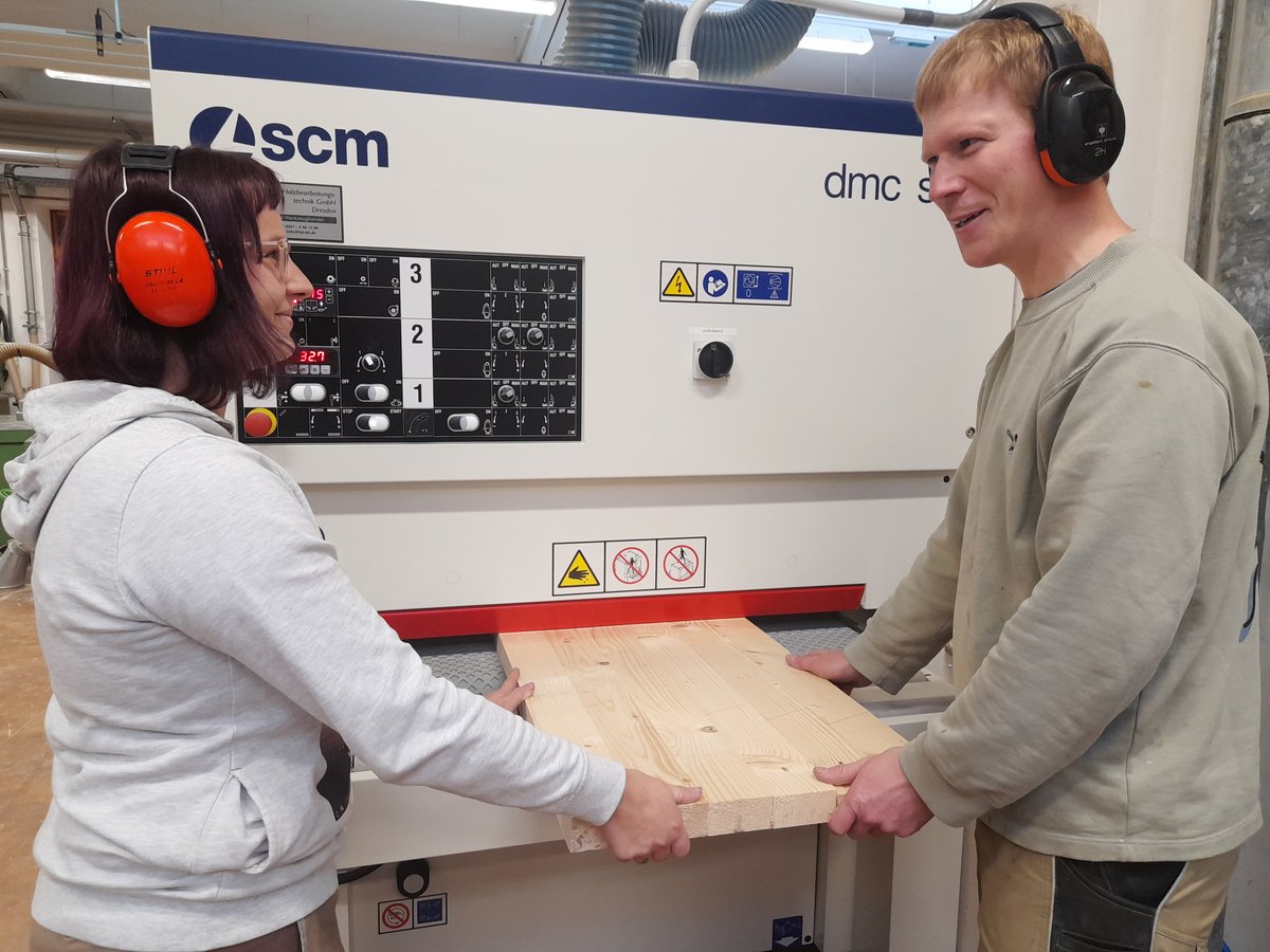 Zwei Personen mit Gehörschutz führen eine große Holzplatte in eine SCM Holzbearbeitungsmaschine ein.