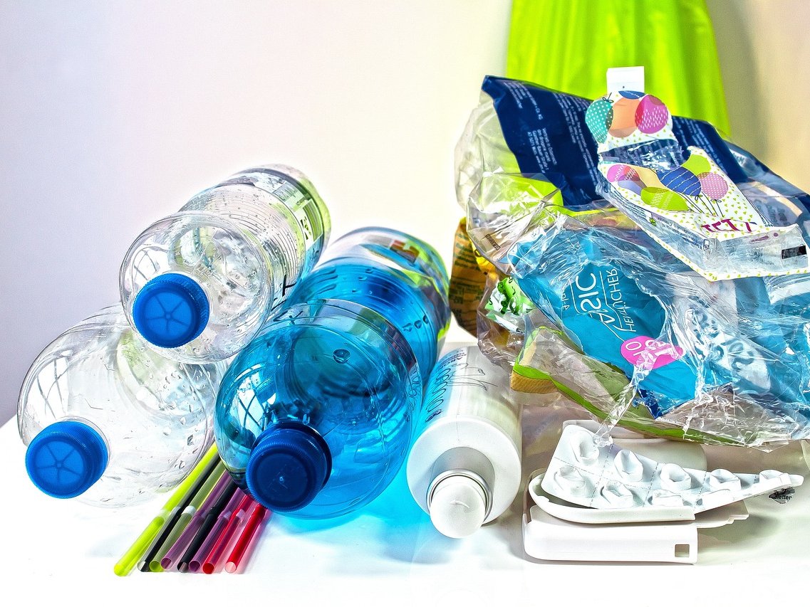 Eine Sammlung von Plastikmüll, darunter Wasserflaschen, bunte Strohhalme, Plastiktüten und ein Blisterpack auf weißem Grund.