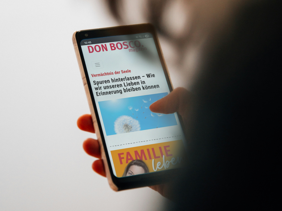Hand hält Smartphone mit einem Artikel aus dem 'DON BOSCO magazin' über Spuren und Erinnerungen.